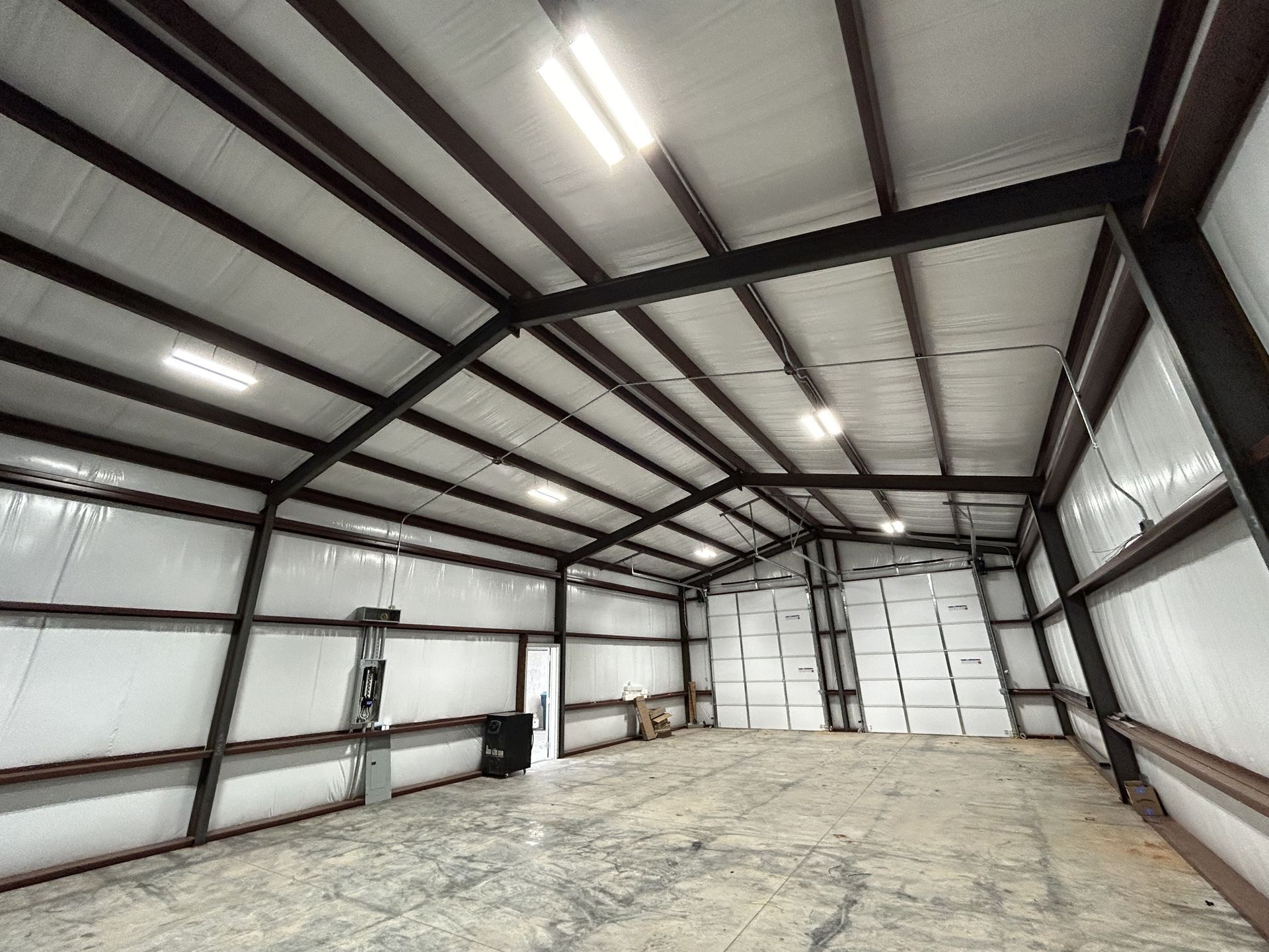 Interior view of a large metal building with a concrete floor. The interior is empty, with bright overhead lighting.