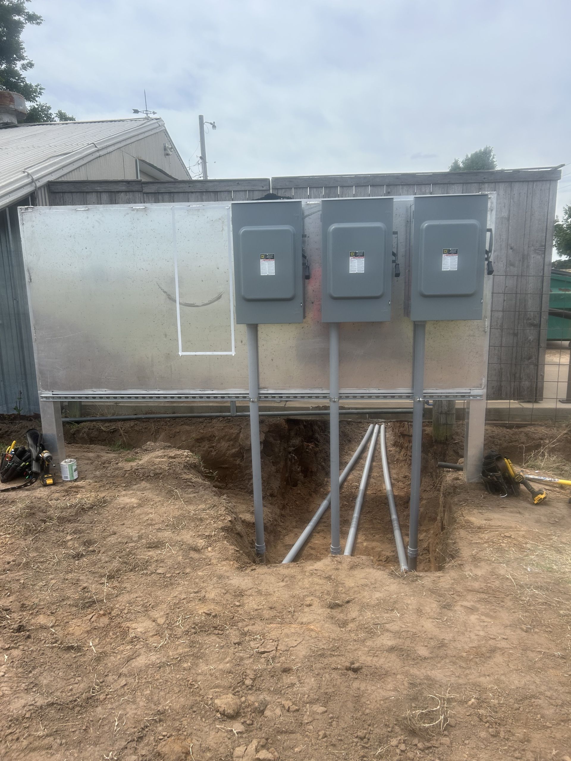 Three gray electrical boxes on metal poles installed outdoors in a construction area.
