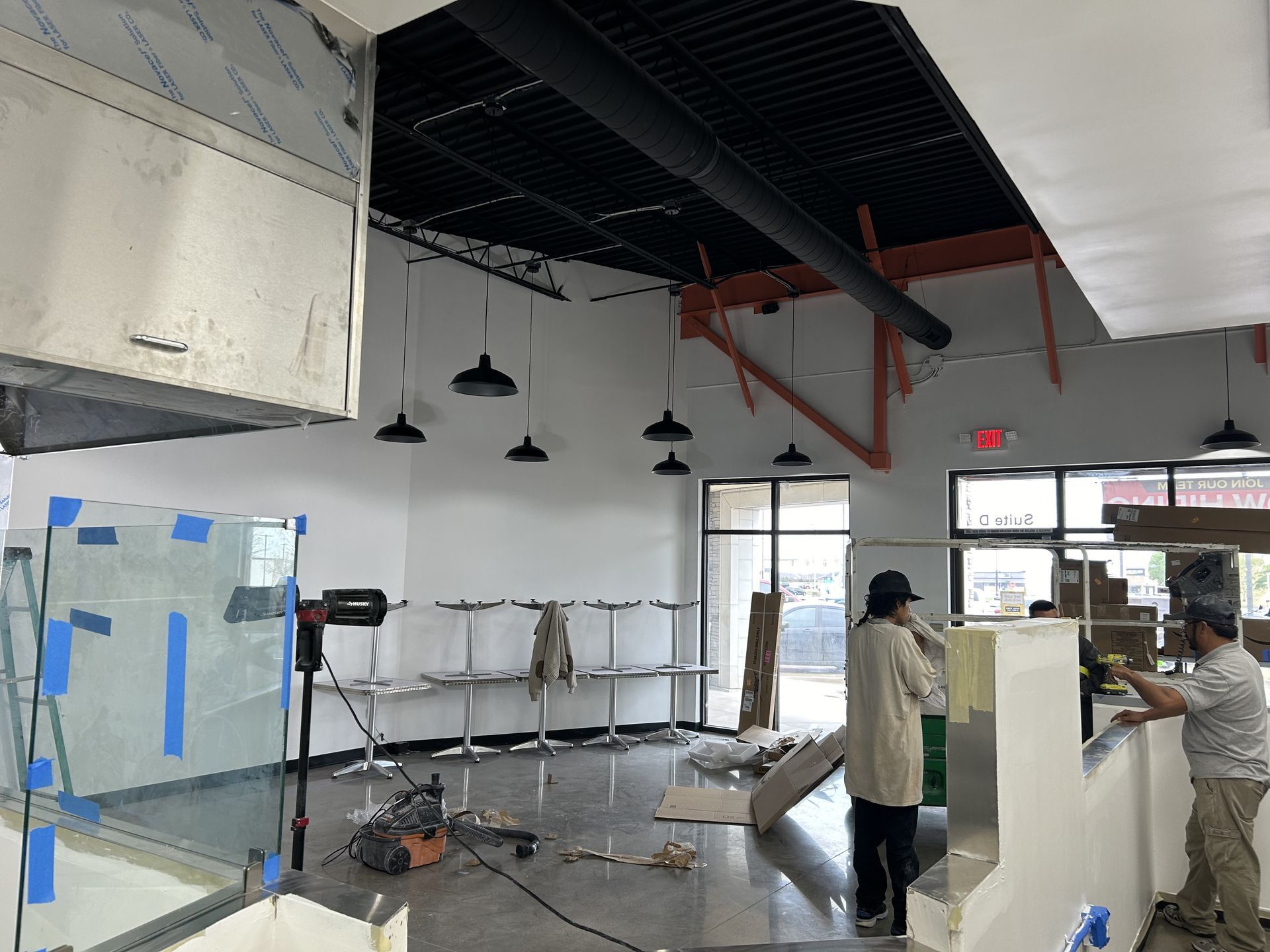 Restaurant interior under construction; workers near a counter, bare tables, and exposed beams.