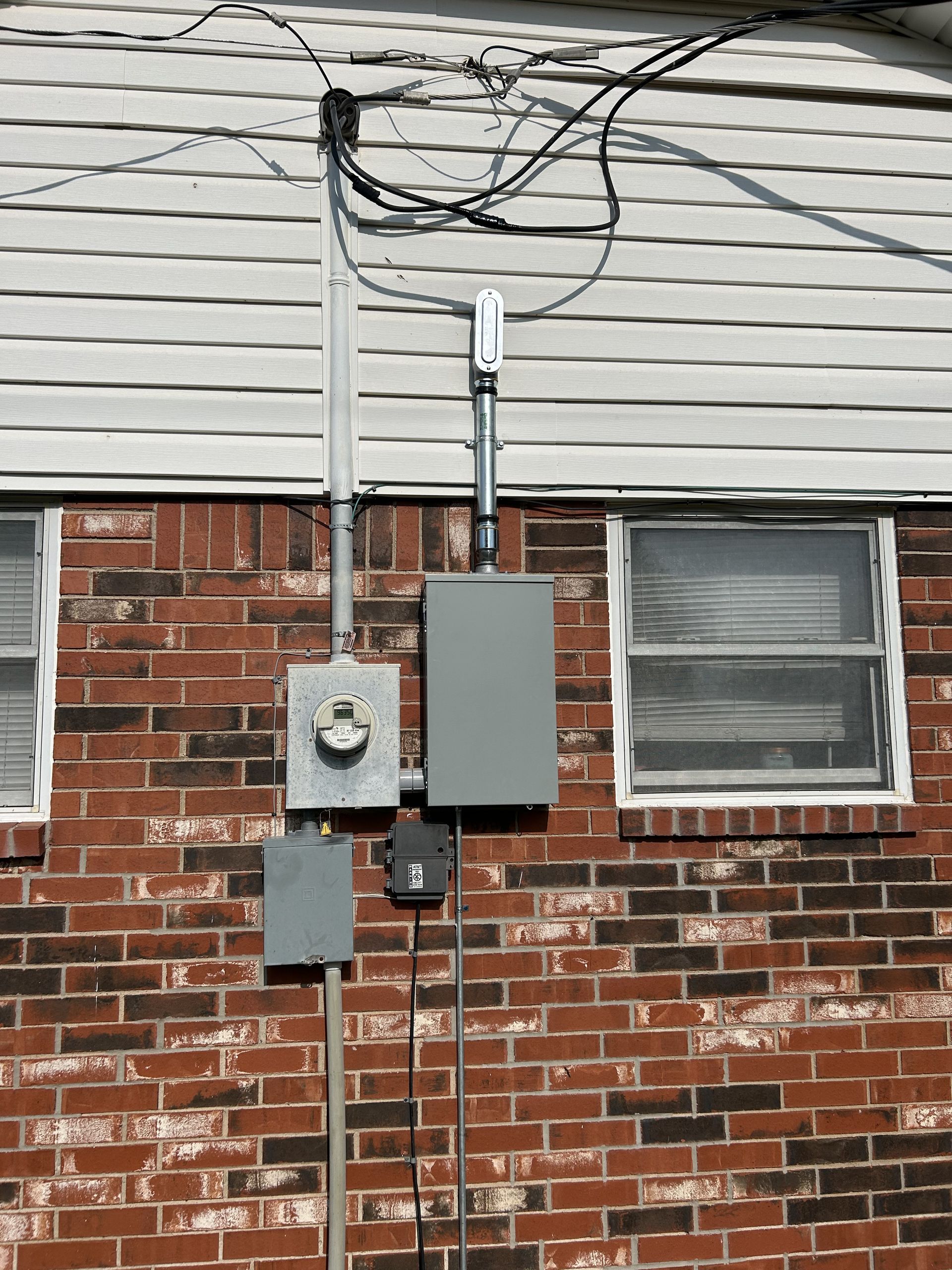 Electrical boxes, pipes, and wiring mounted on a red brick wall. Gray boxes with metal conduit.