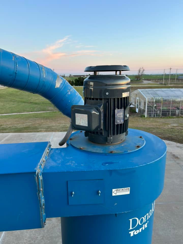 Blue industrial dust collector on a flat surface, with a motor and blue tubing against a sunset sky.