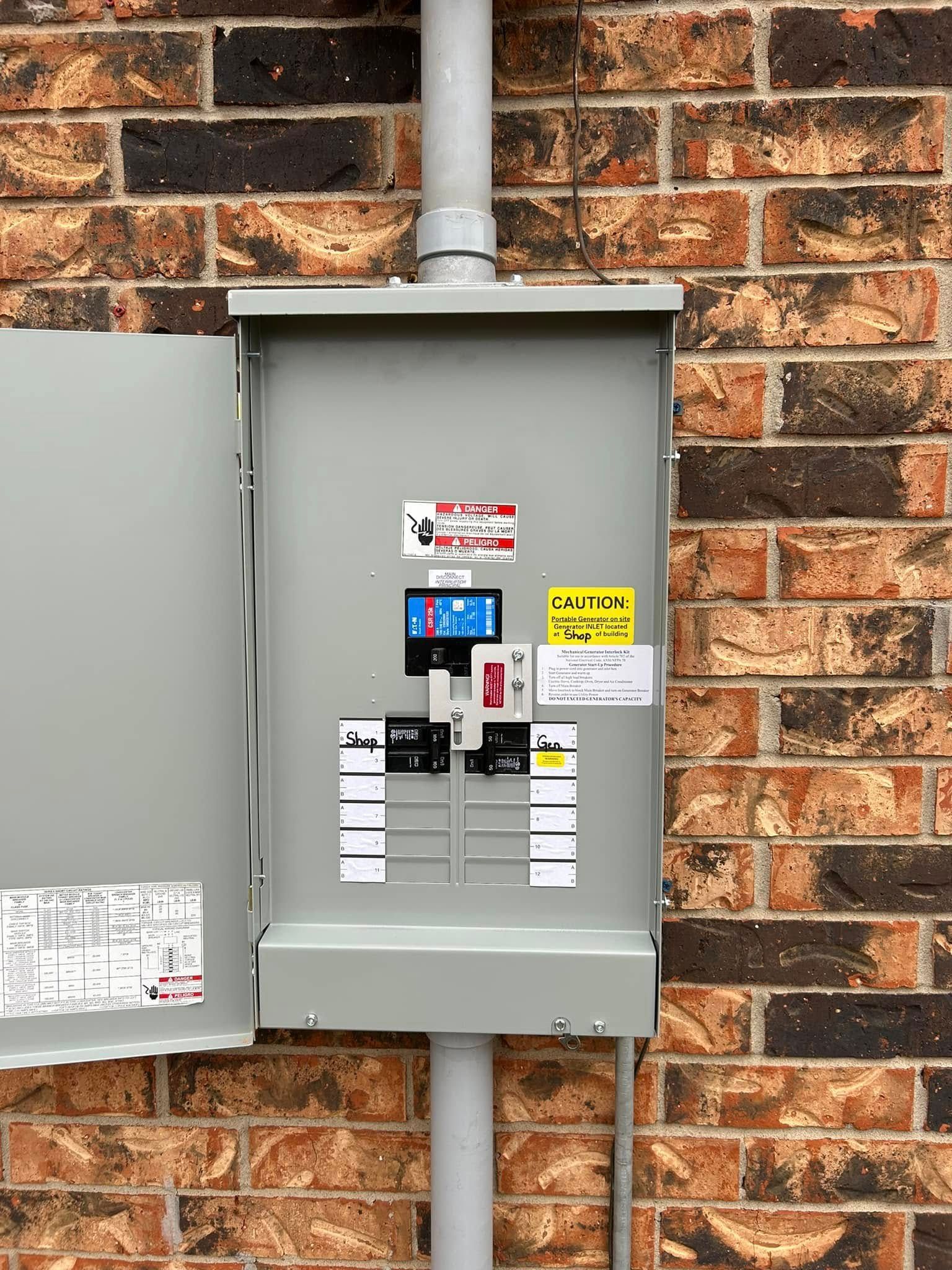 Open electrical box on a brick wall. Grey metal with labels, conduit running above and below.