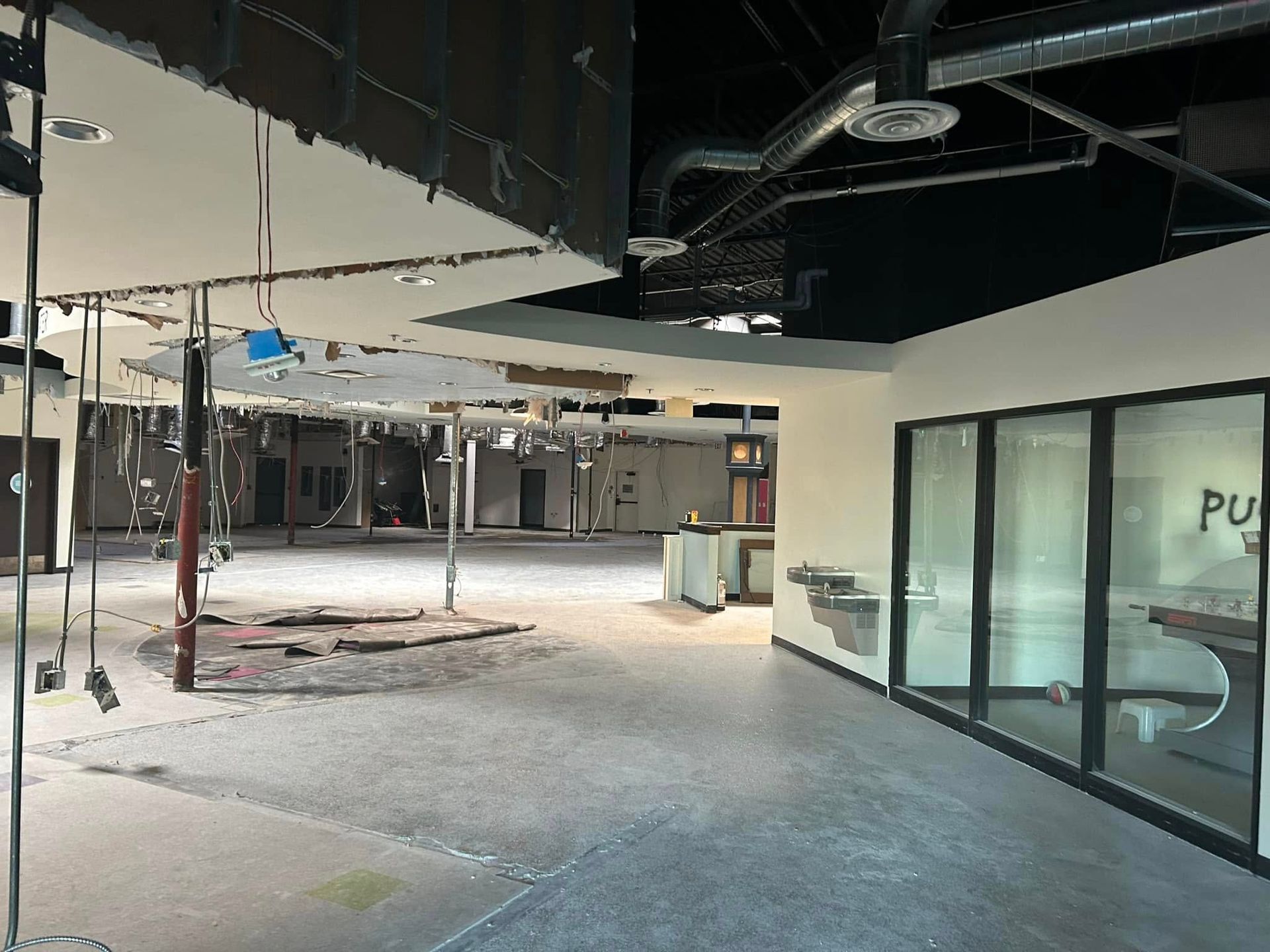 Interior of a commercial space under construction; ceiling and walls damaged; bare concrete floor.