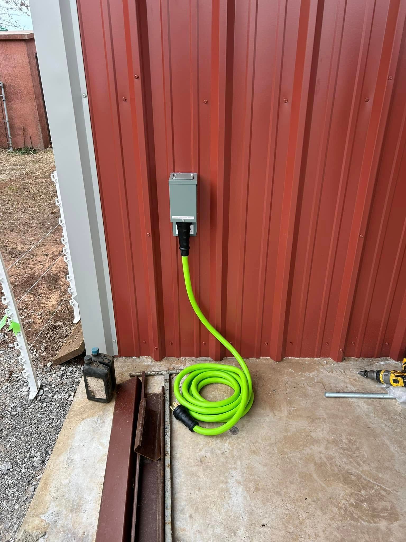 Electric vehicle charger on a red metal building wall, green cable coiled on concrete ground.