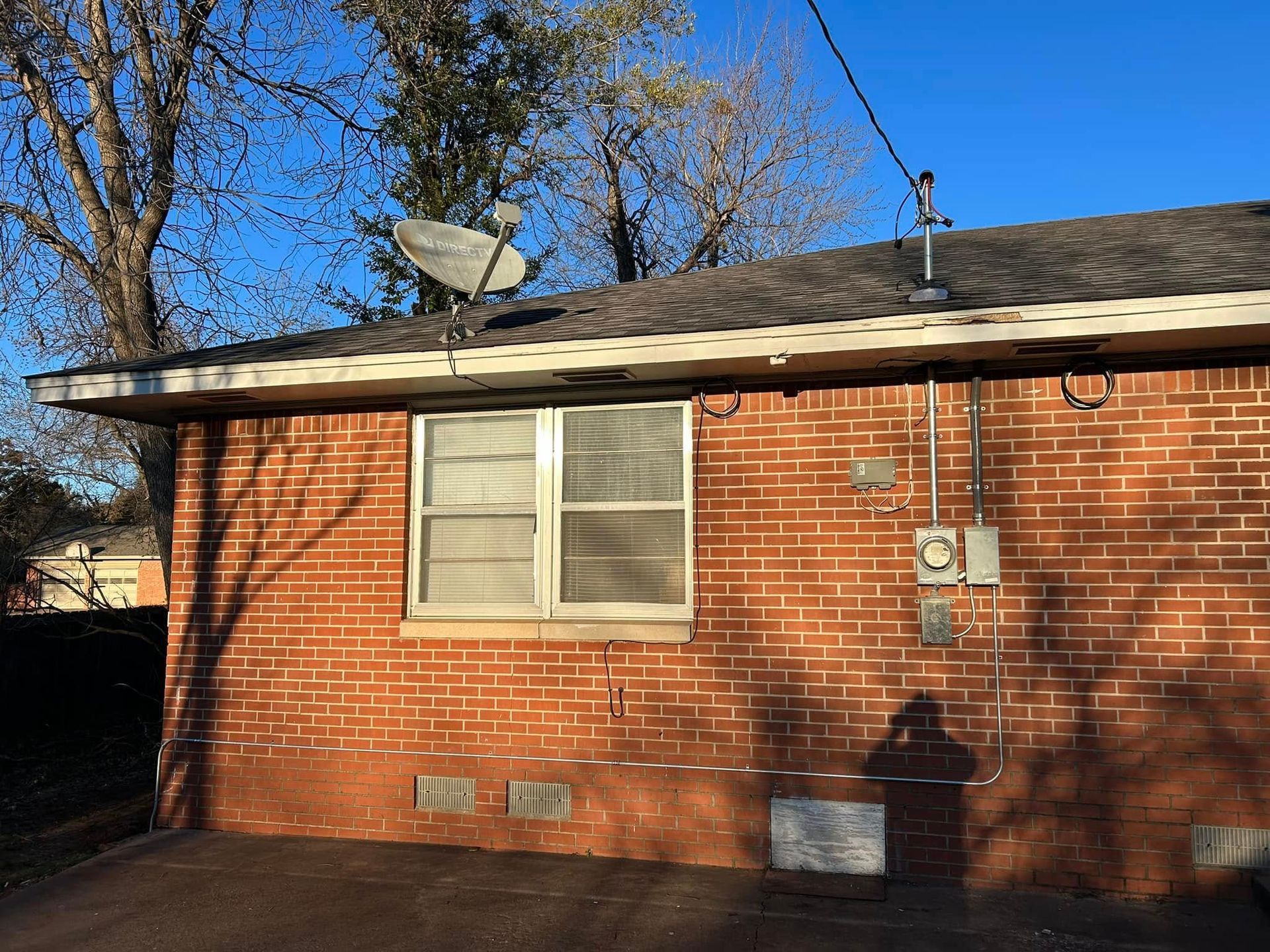 Brick building exterior with window, satellite dish, and electrical boxes against a blue sky.