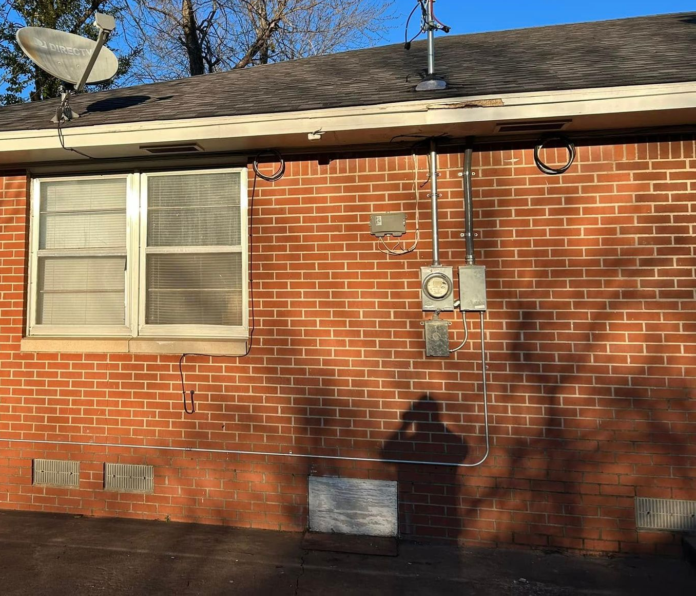 Red brick building exterior with a window, electrical boxes, and satellite dish.