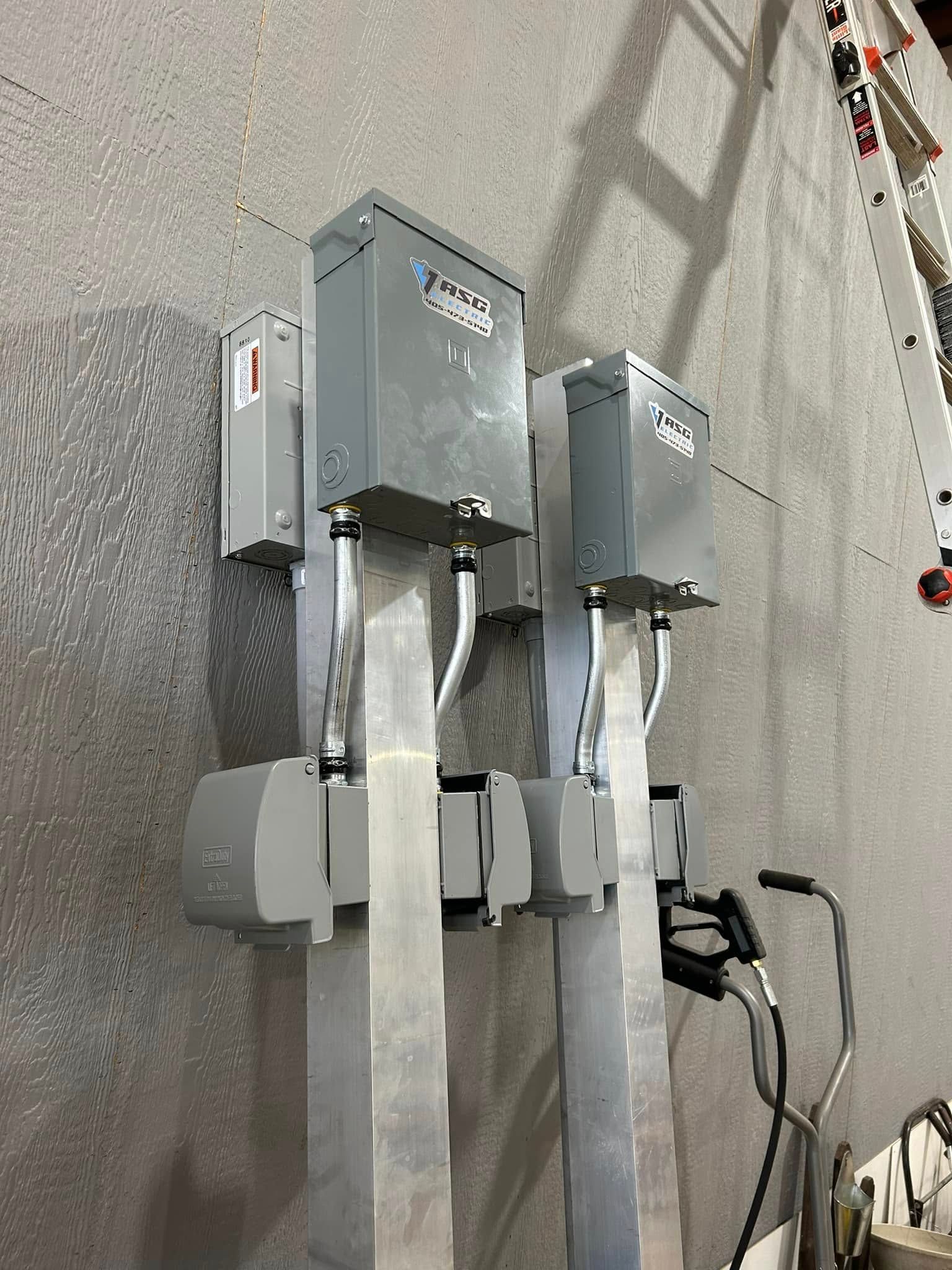 Wall-mounted electric vehicle charging stations, silver and gray, with cables and a gray wall.