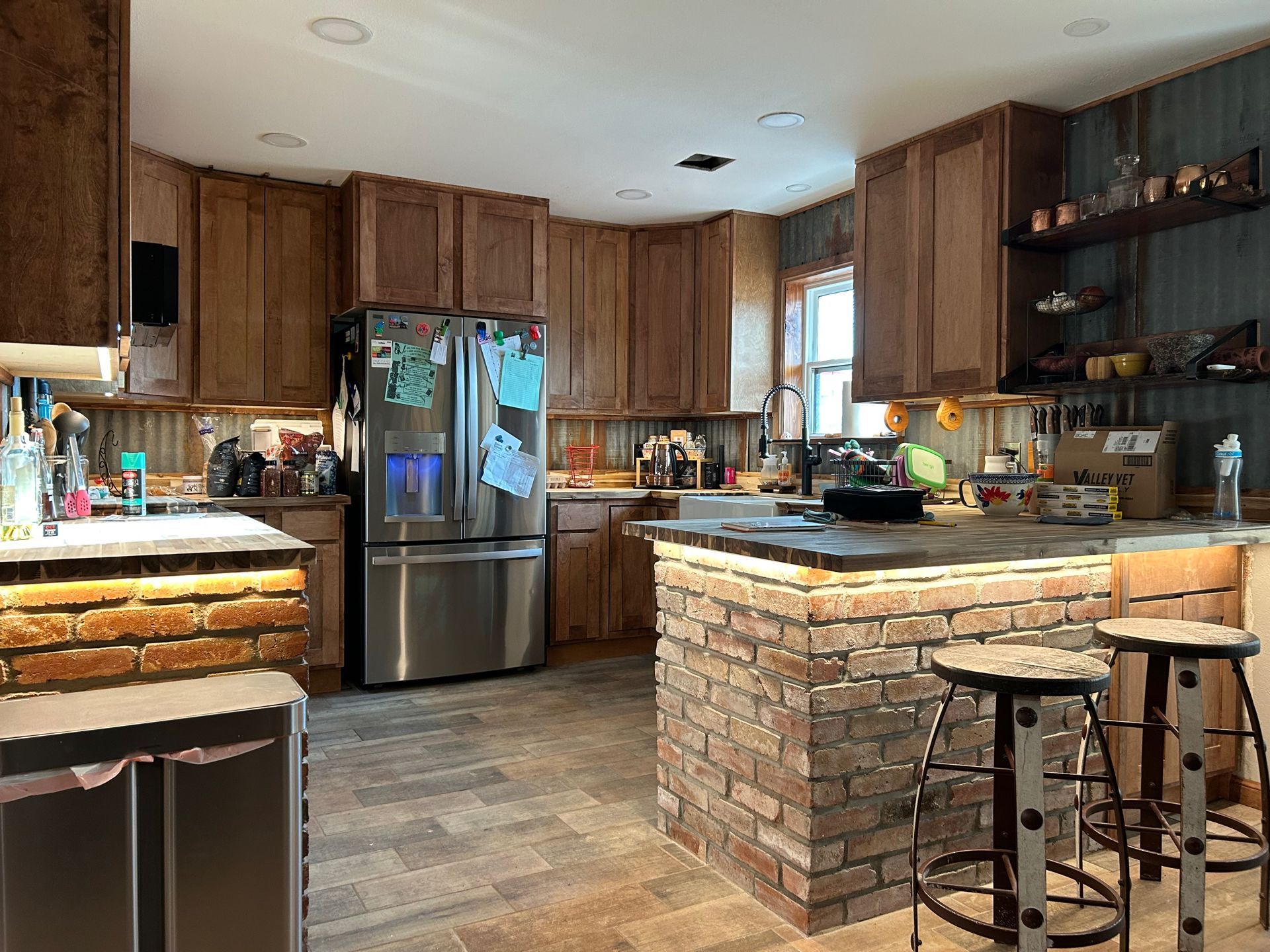 Kitchen with wood cabinets, stainless steel refrigerator, brick accents, and bar stools.