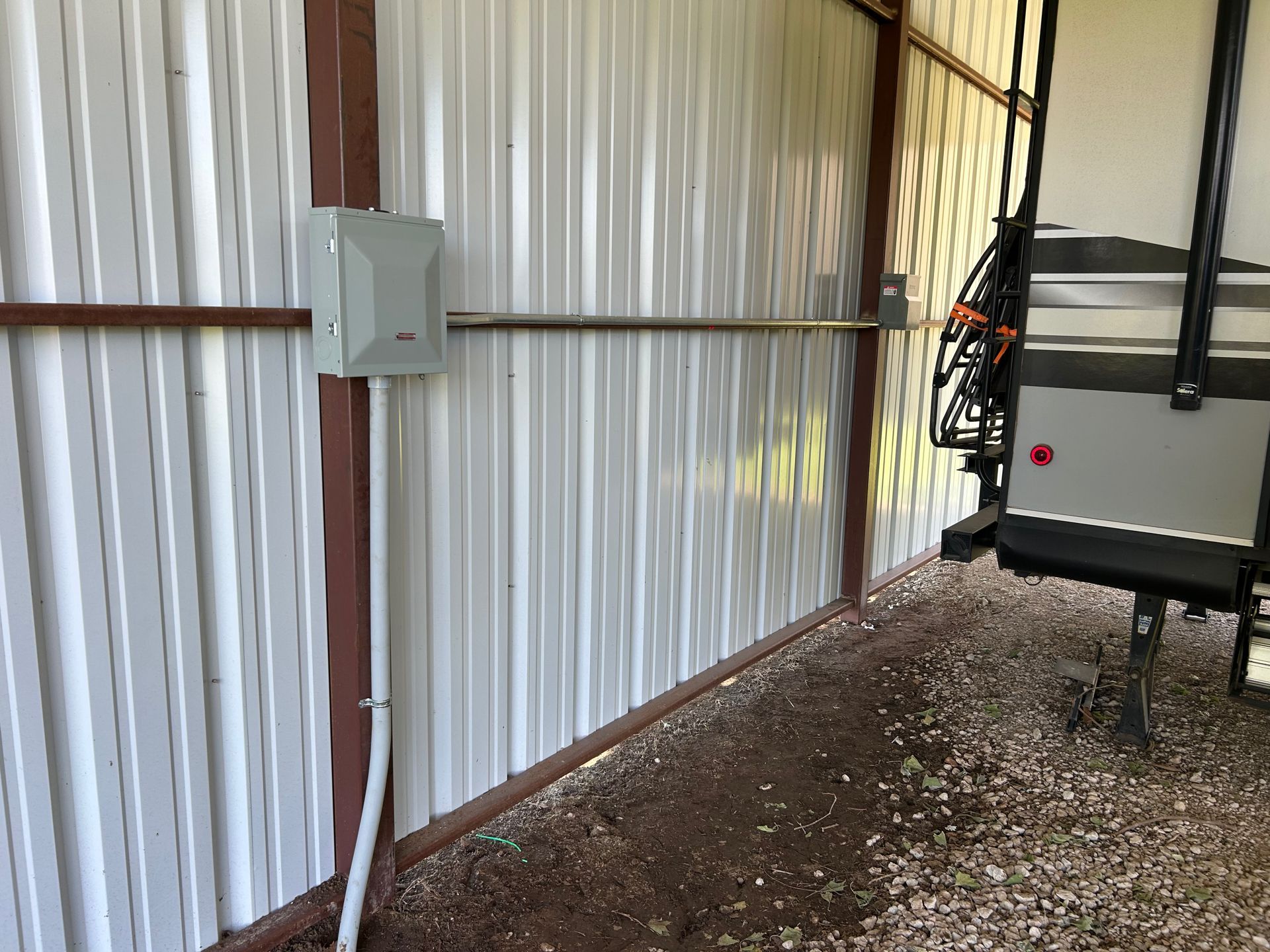 Electrical box and conduit on a corrugated metal wall, near a parked RV.