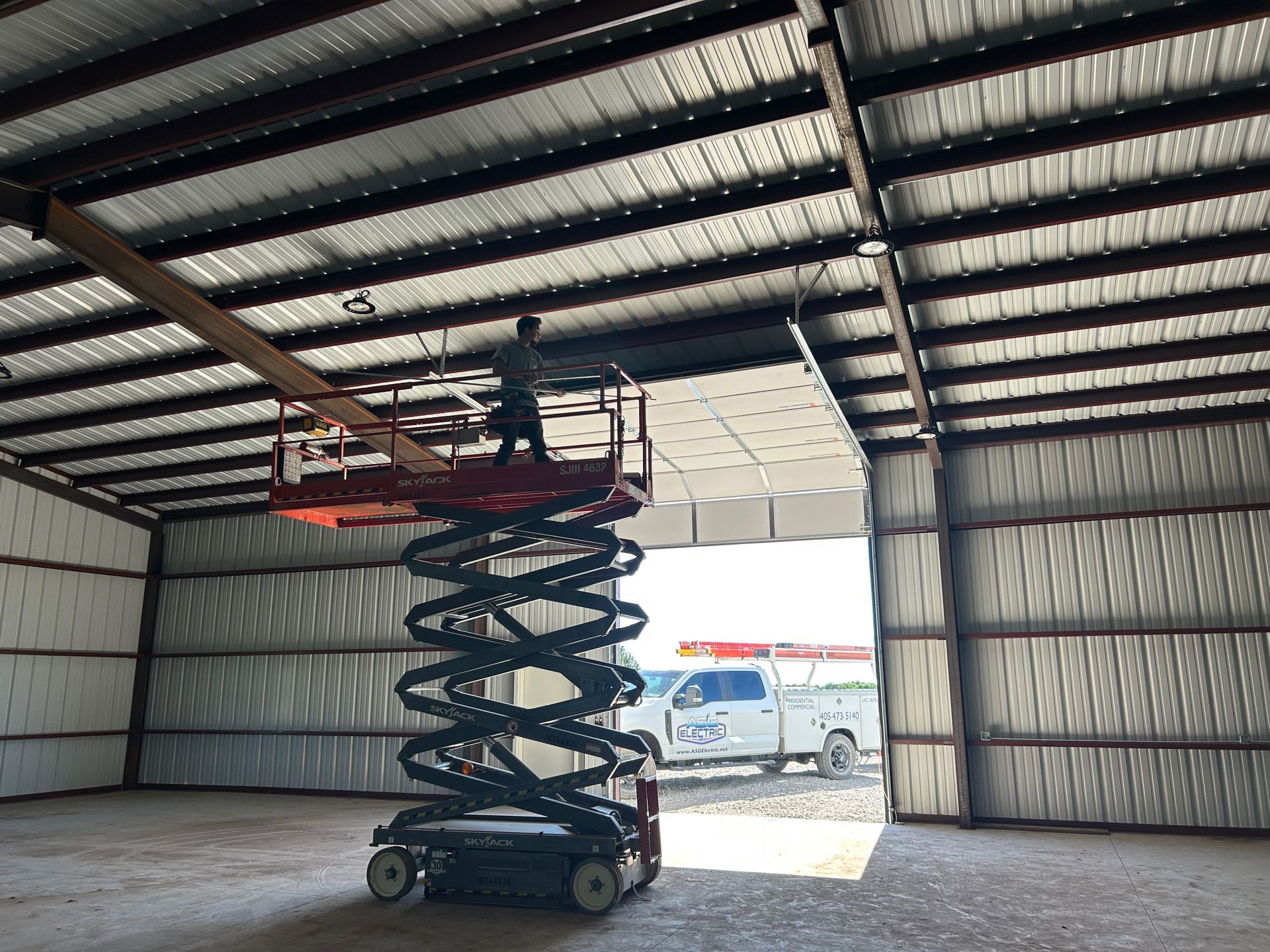 Person on lift installing panels inside a metal building with a truck visible outside the open door.