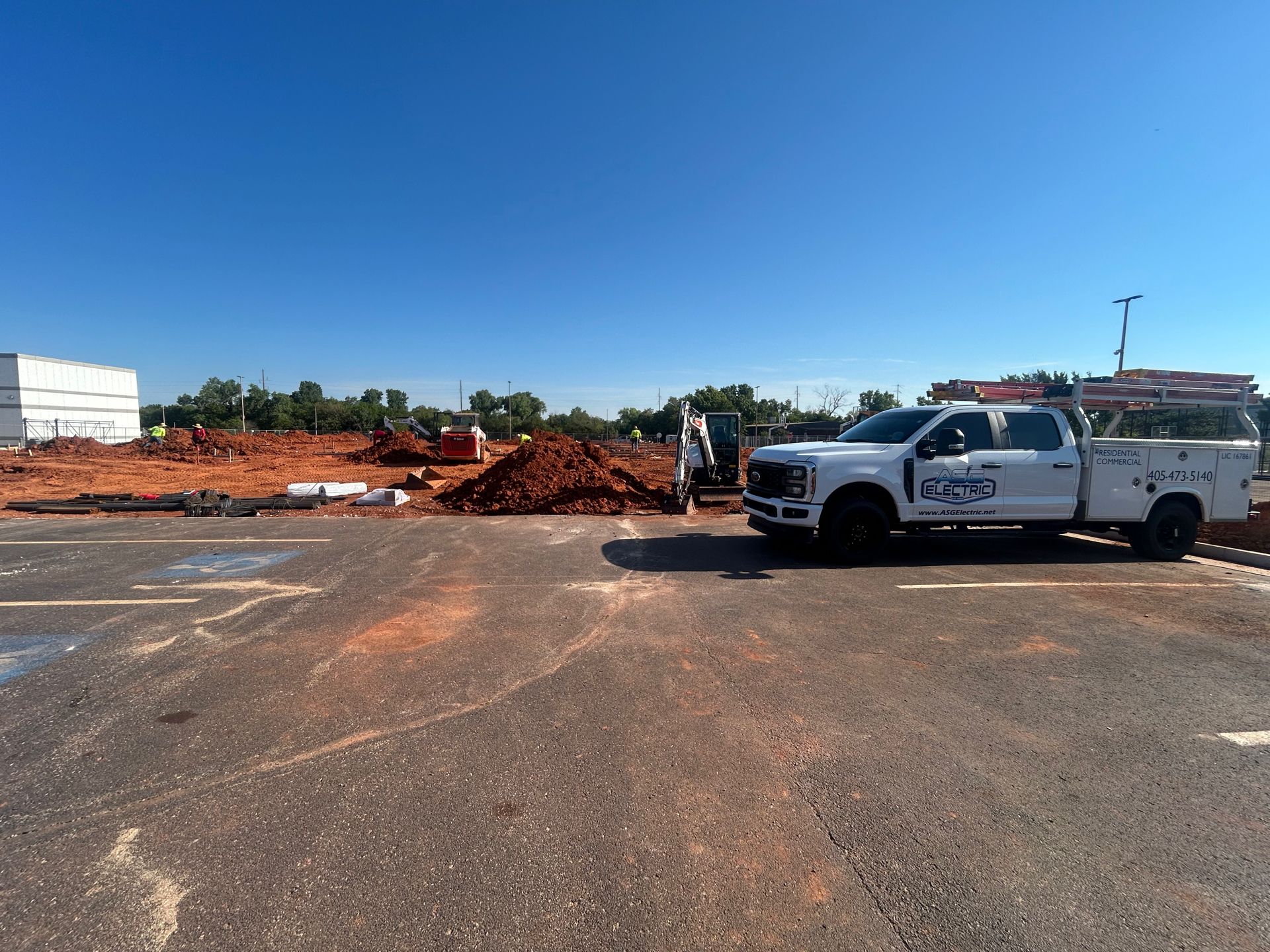 White work truck parked at construction site; red dirt and clear sky.
