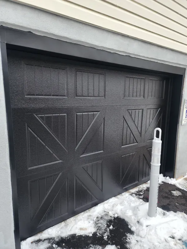 A black garage door is sitting in the snow next to a white pole.