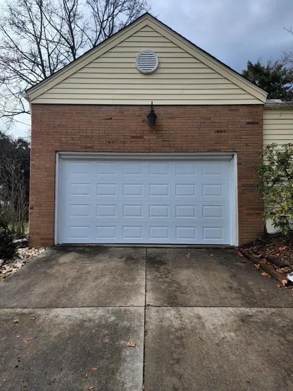 A white garage door is sitting in front of a brick house.