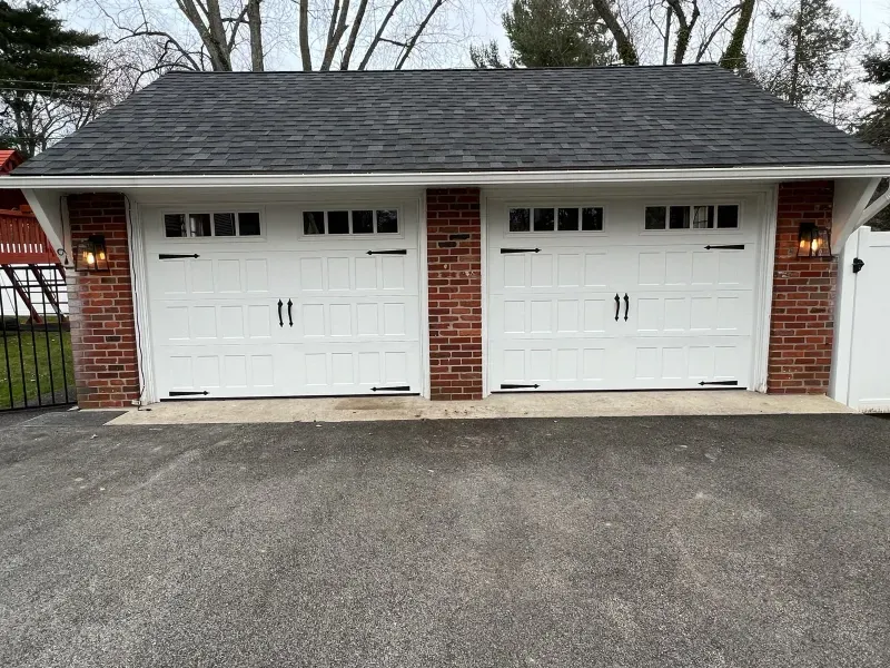 A garage with two white garage doors and a brick wall