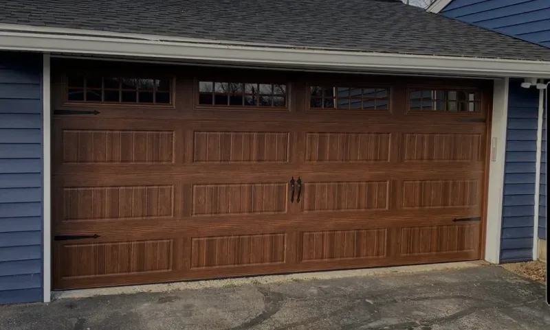 A large wooden garage door is sitting in front of a blue house.
