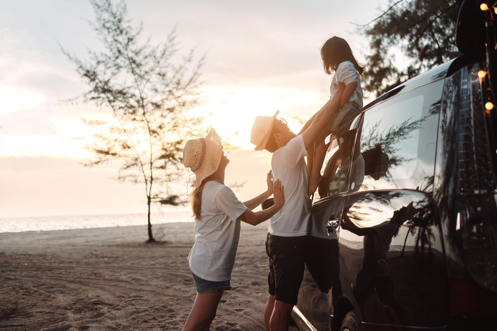 A family is standing next to a car on the beach at sunset.