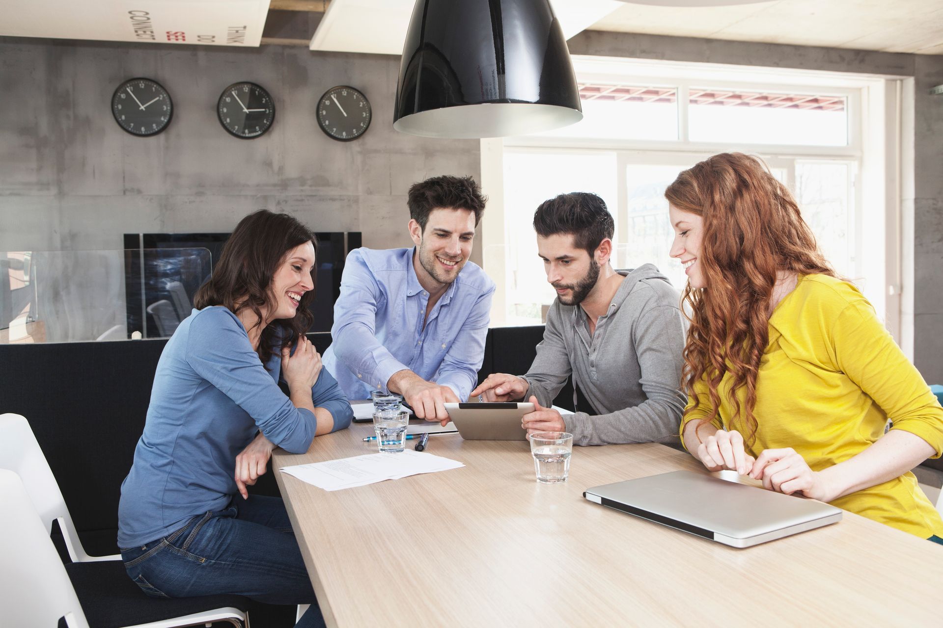 A group of people are sitting around a table looking at a tablet.