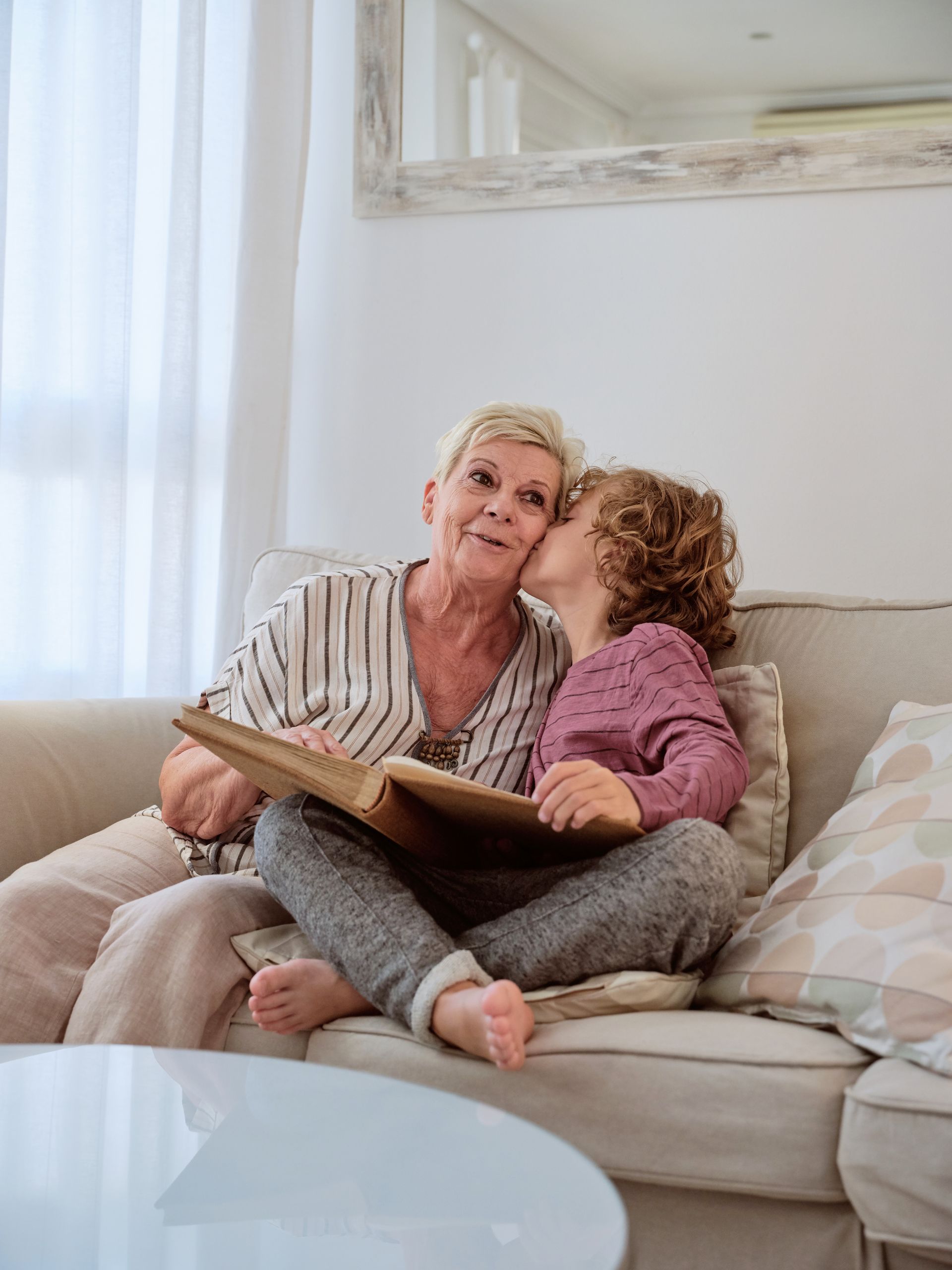 A little girl is kissing an older woman on the cheek while sitting on a couch.