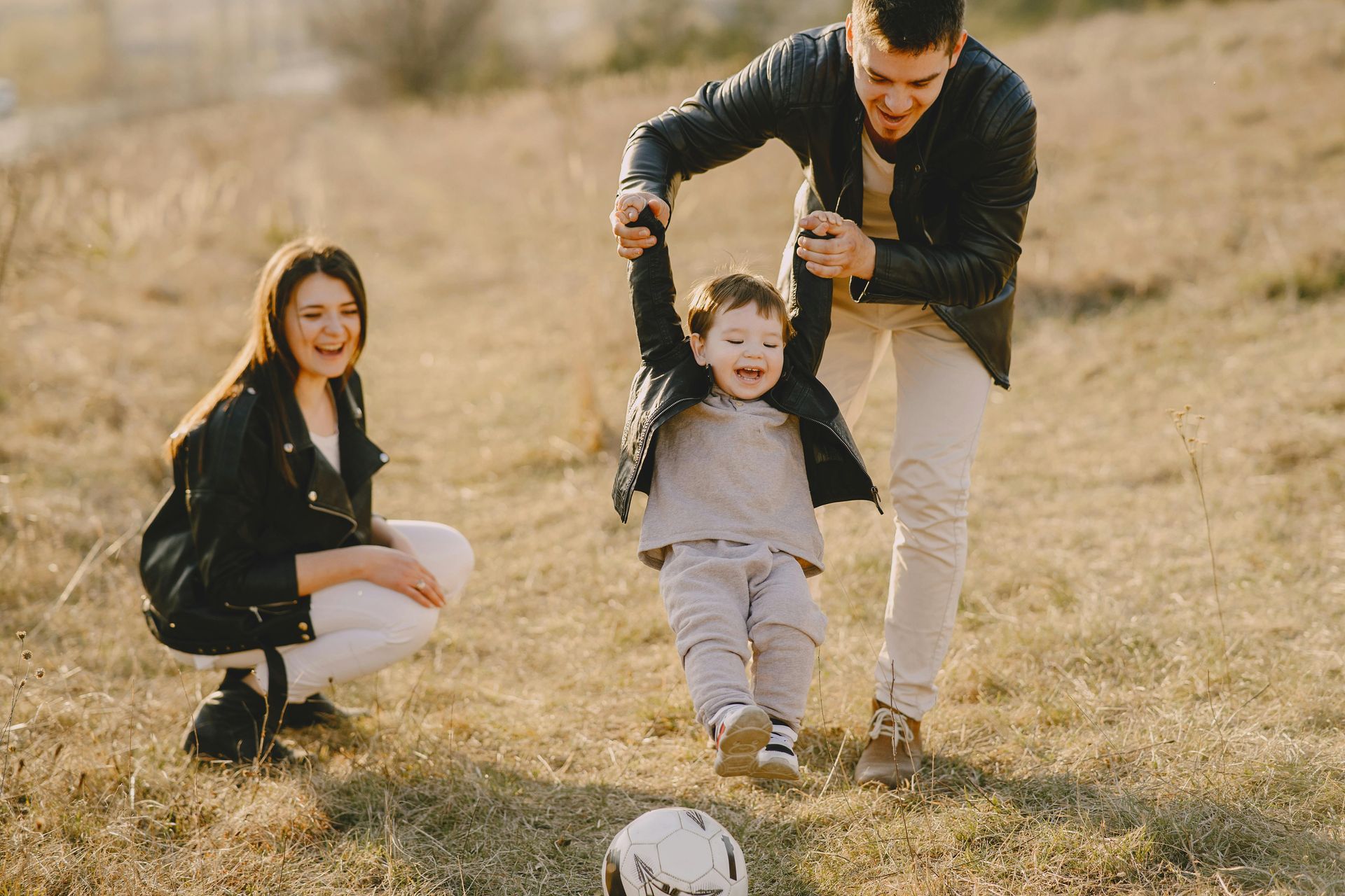 A family is playing with a soccer ball in a field.