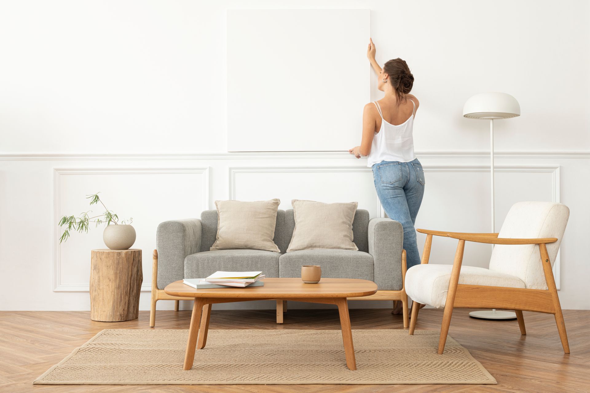 A woman is hanging a picture on a wall in a living room.