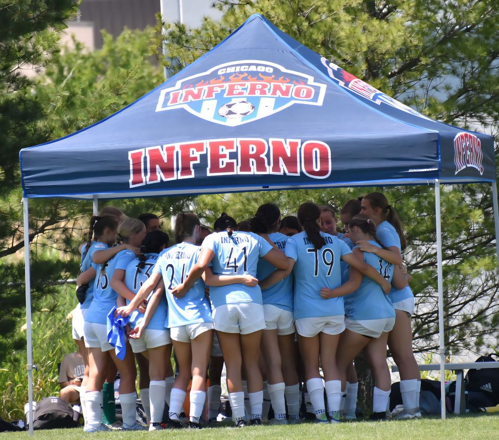 Soccer team in light blue jerseys huddled under a blue canopy with 