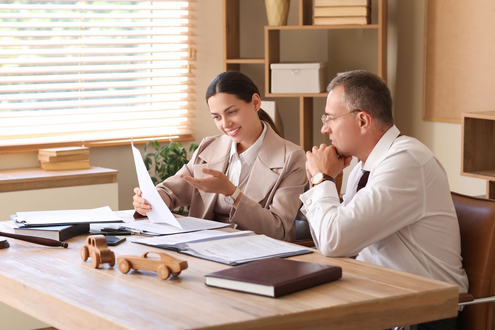 Woman and man reviewing documents at a desk in an office. Wooden cars on the desk.