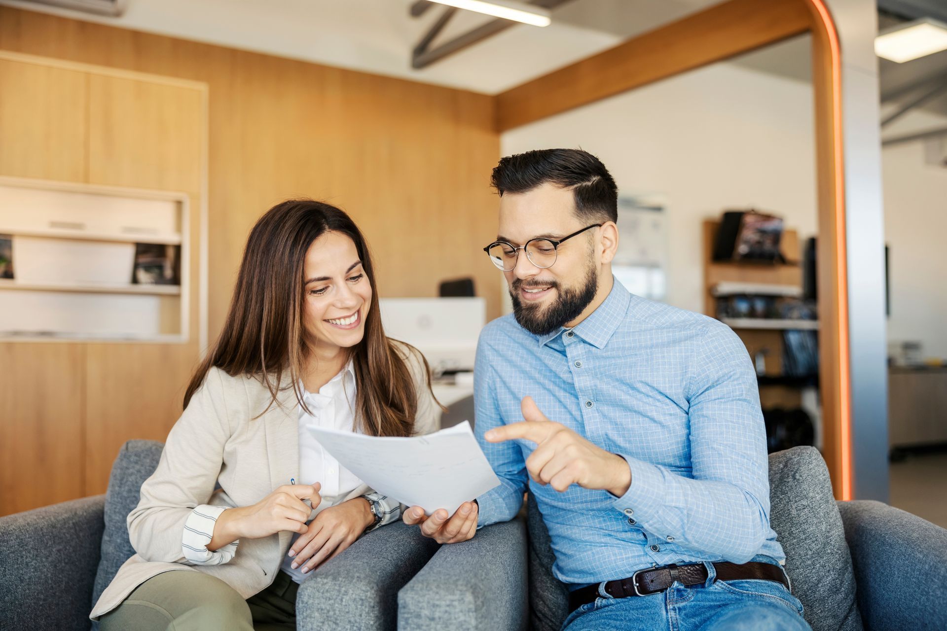 Woman and man smiling, reviewing documents in an office setting.