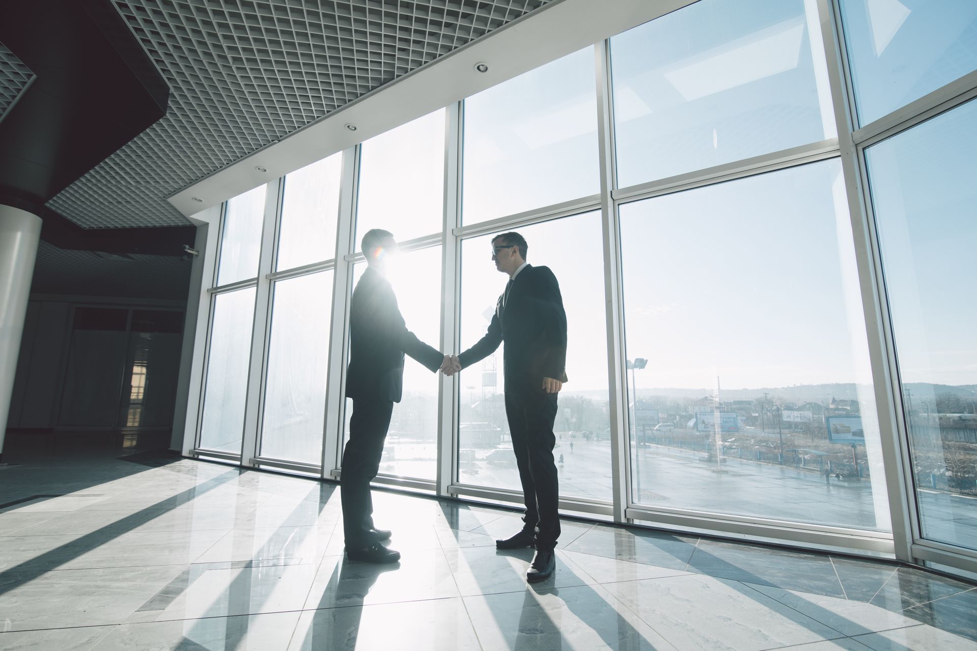 Two businesspeople shaking hands in a modern office with large windows, sunlight, and city views. Two businesspeople shaking hands in a modern office with large windows, sunlight, and city views.
