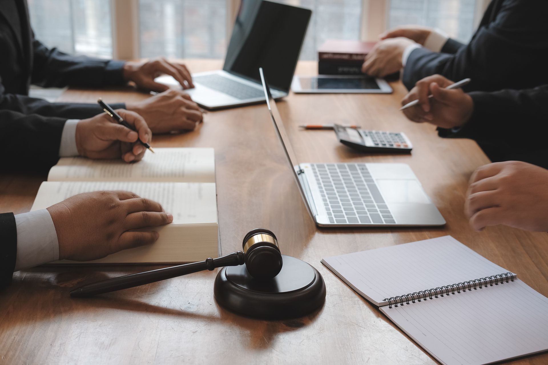 Meeting with legal professionals at a table with laptops, notebooks, a gavel, and a calculator. Meeting with legal professionals at a table with laptops, notebooks, a gavel, and a calculator.