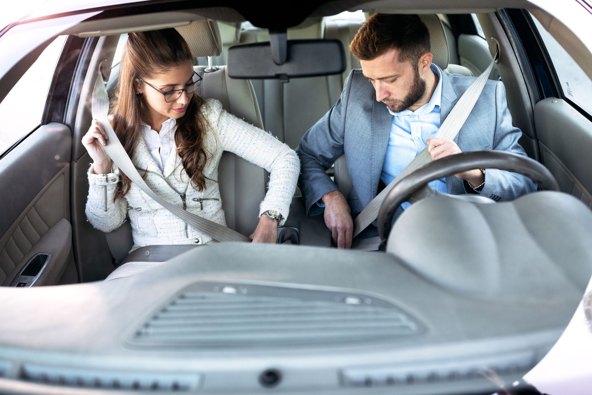 Woman and man inside a car, buckling seatbelts.