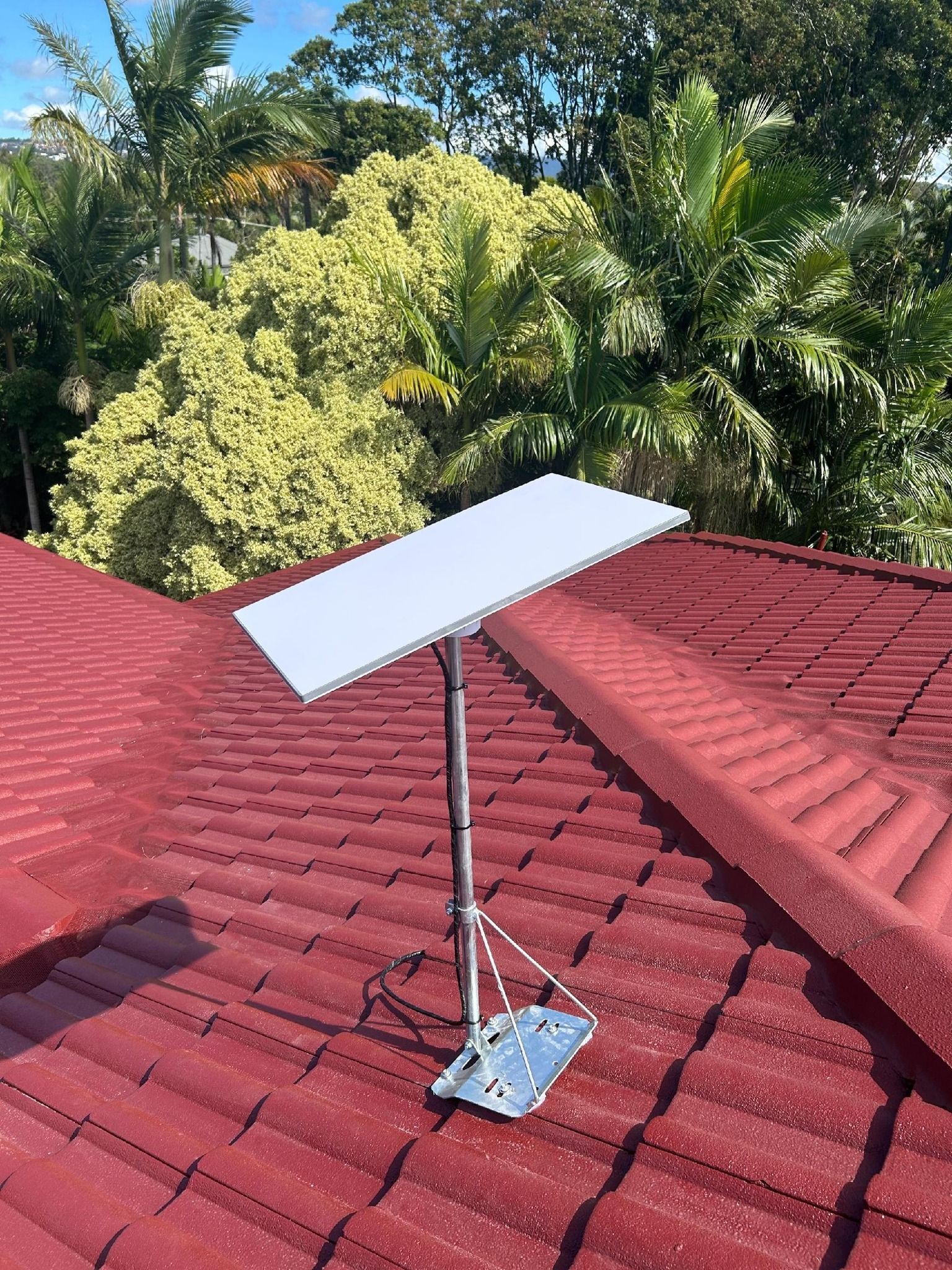 A satellite dish is sitting on top of a red tiled roof.