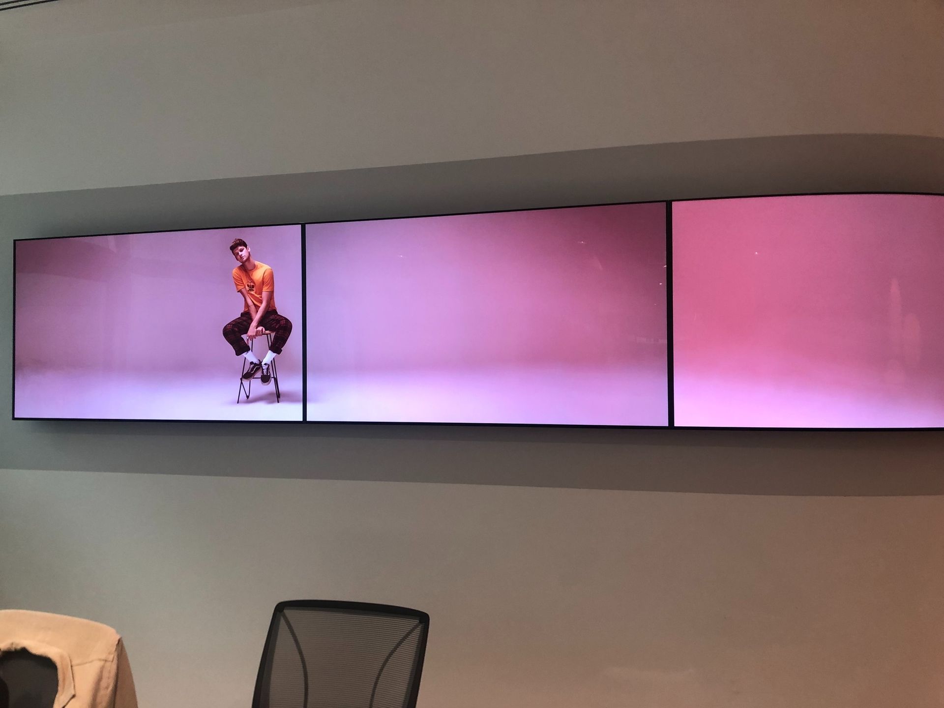 A man is standing on a skateboard in front of three screens on a wall.