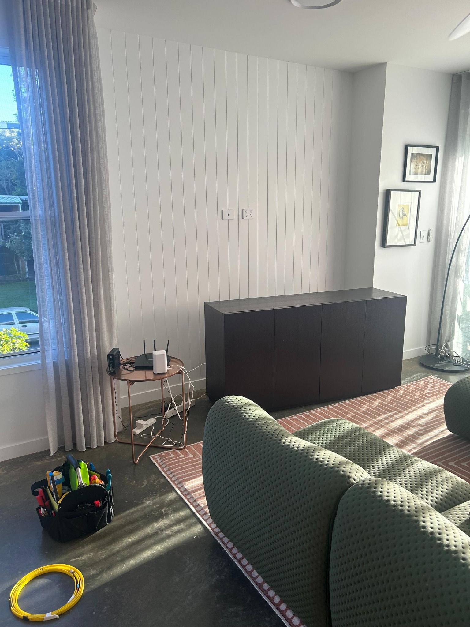 A living room with a green couch , a dresser , and a window.