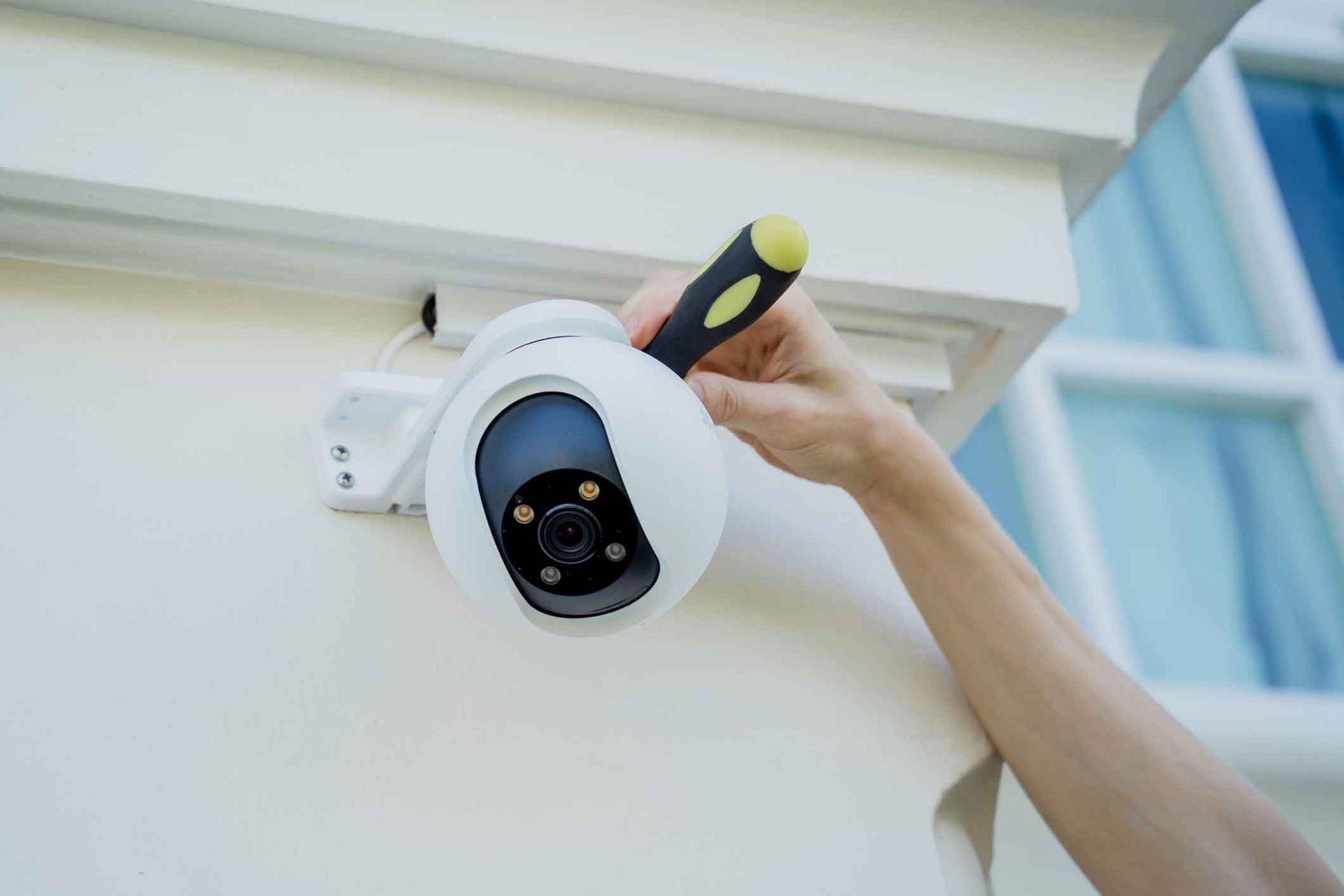 A person is installing a security camera on the side of a building.