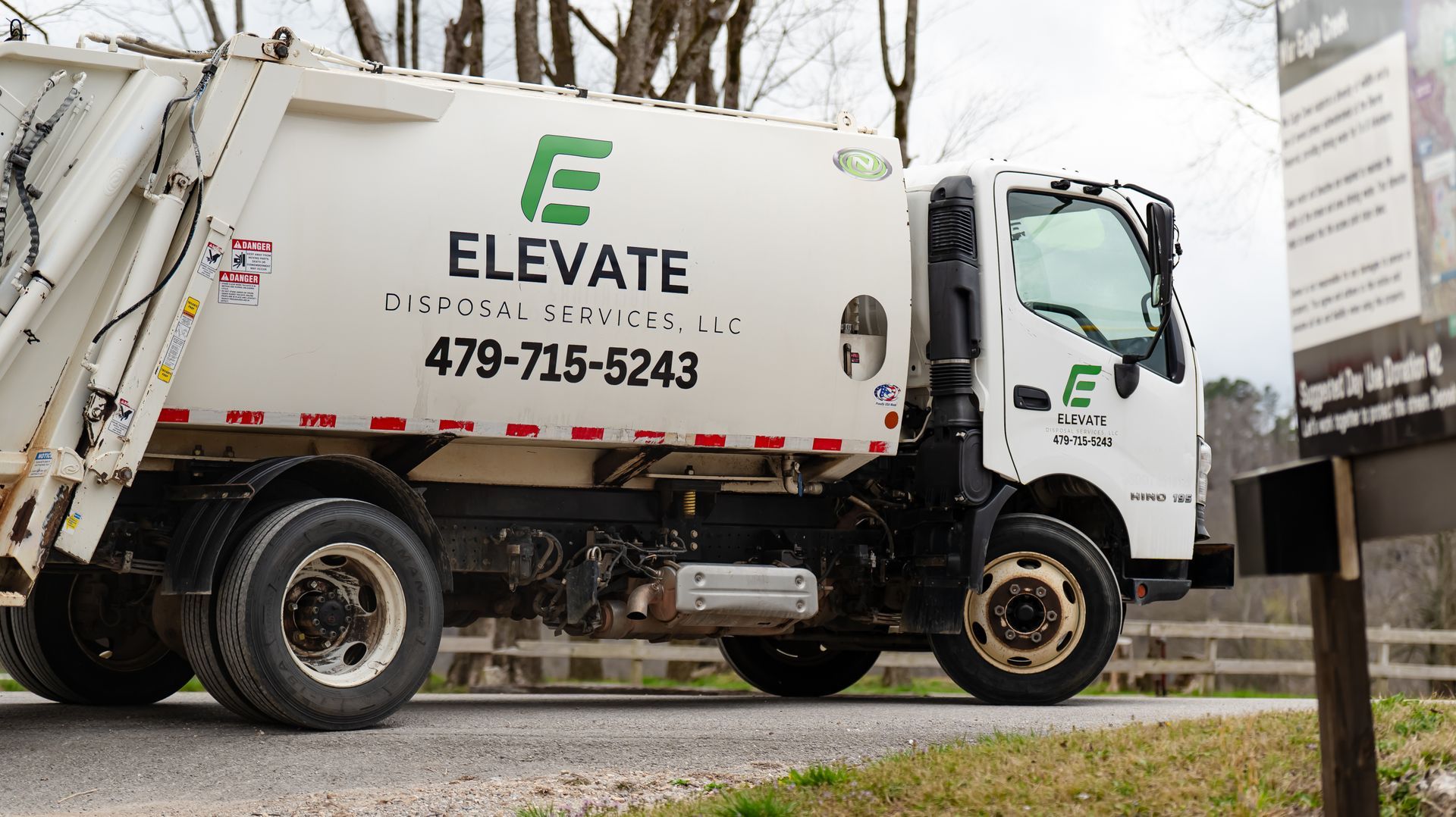 A blue dumpster filled with junk is sitting on the side of the road.