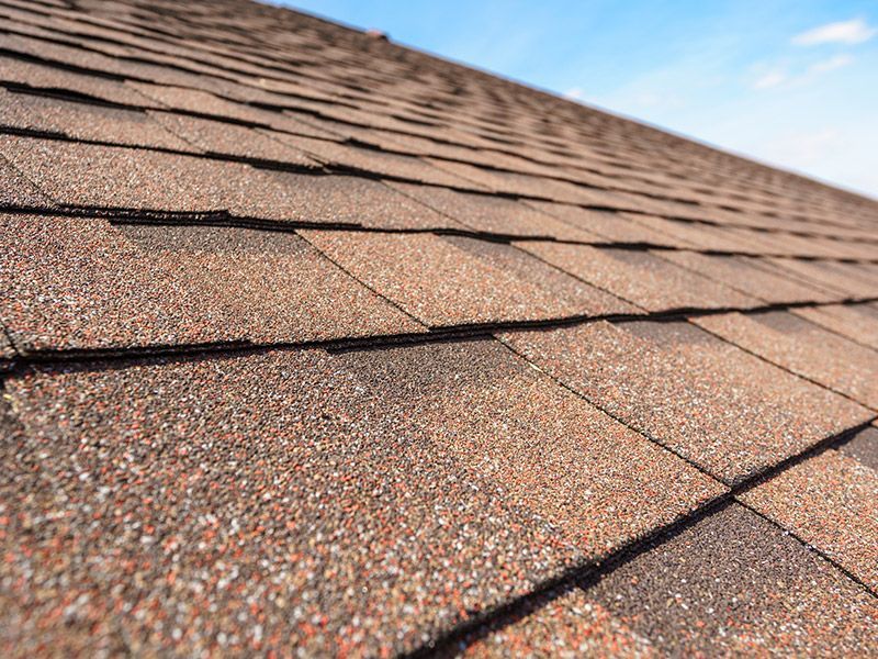 A close up of a roof with shingles against a blue sky.