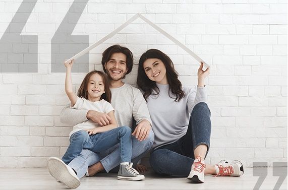 A family is sitting on the floor in front of a brick wall.