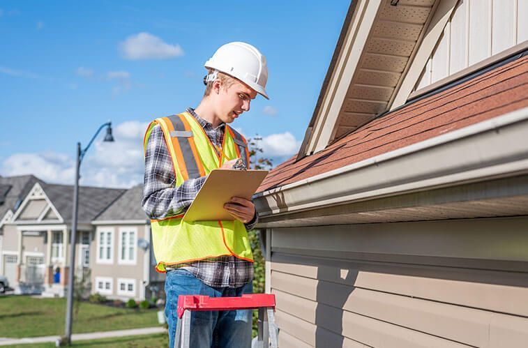 A man is standing on a ladder looking at a gutter on a house.