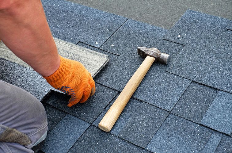 A person is installing shingles on a roof with a hammer.