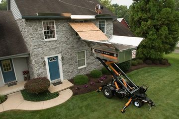 A man is working on the roof of a house with a trailer attached to it.