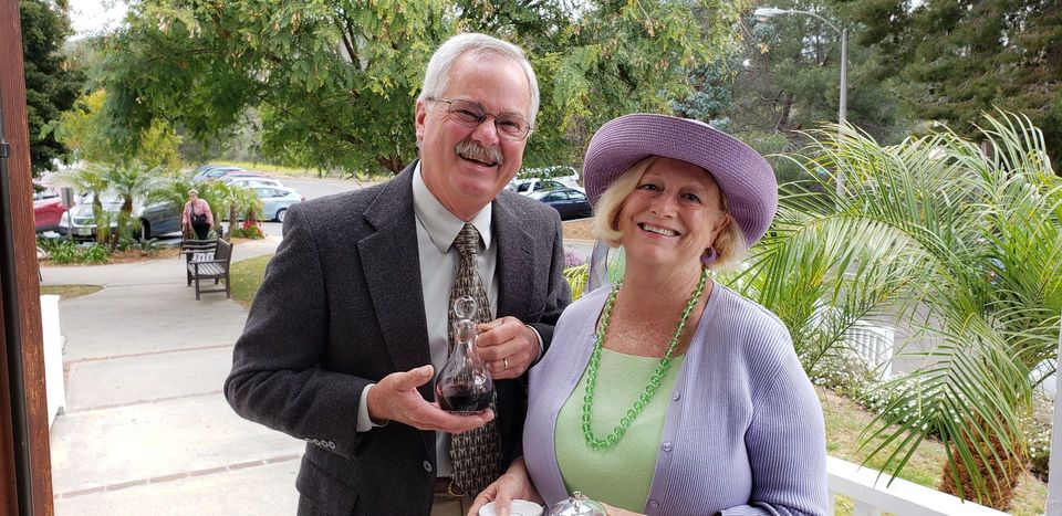 A man in a suit and tie is standing next to a woman in a purple hat.