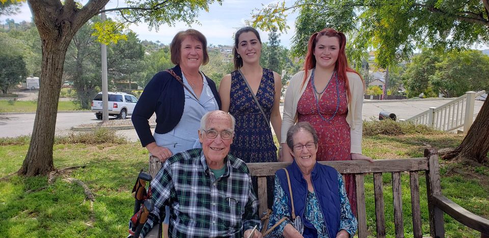 A group of people are posing for a picture while sitting on a bench in a park.