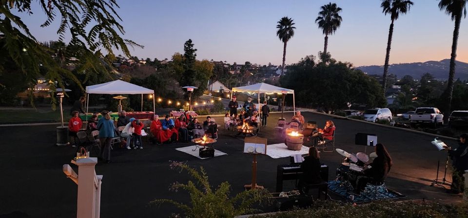 A group of people are sitting around a fire pit in a parking lot.