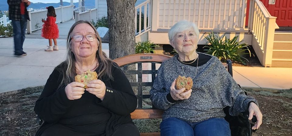 Two women are sitting on a bench eating sandwiches.
