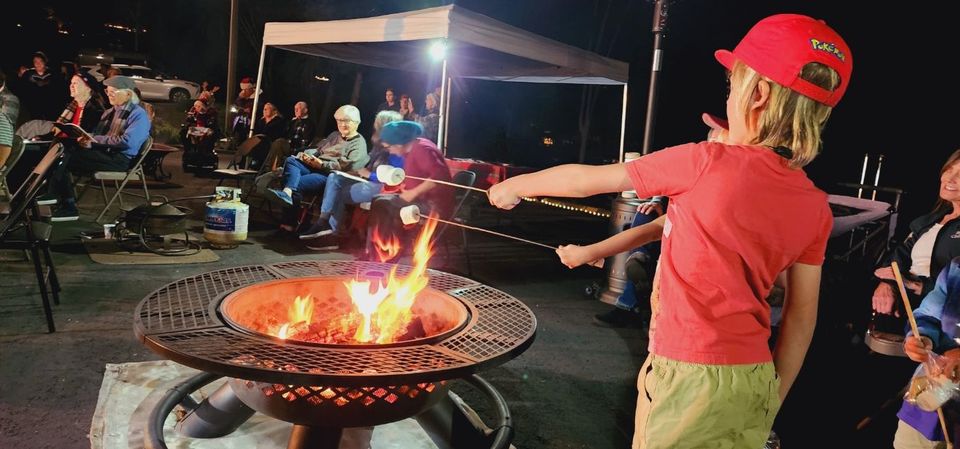 A group of people are sitting around a fire pit at night.