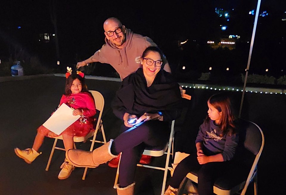 A family is sitting around a fire playing a video game.