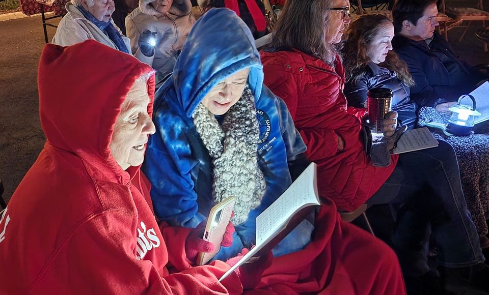 A group of people are sitting in a row reading a book.