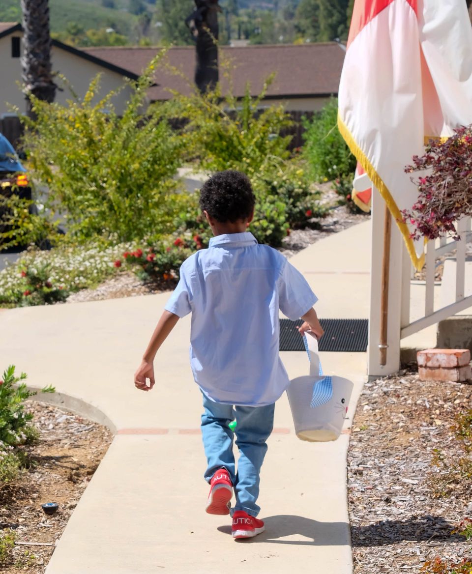 A young boy is walking down a sidewalk with a bucket in his hand.