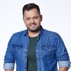 Een man met een baard draagt ​​een spijkerhemd en een groen shirt.