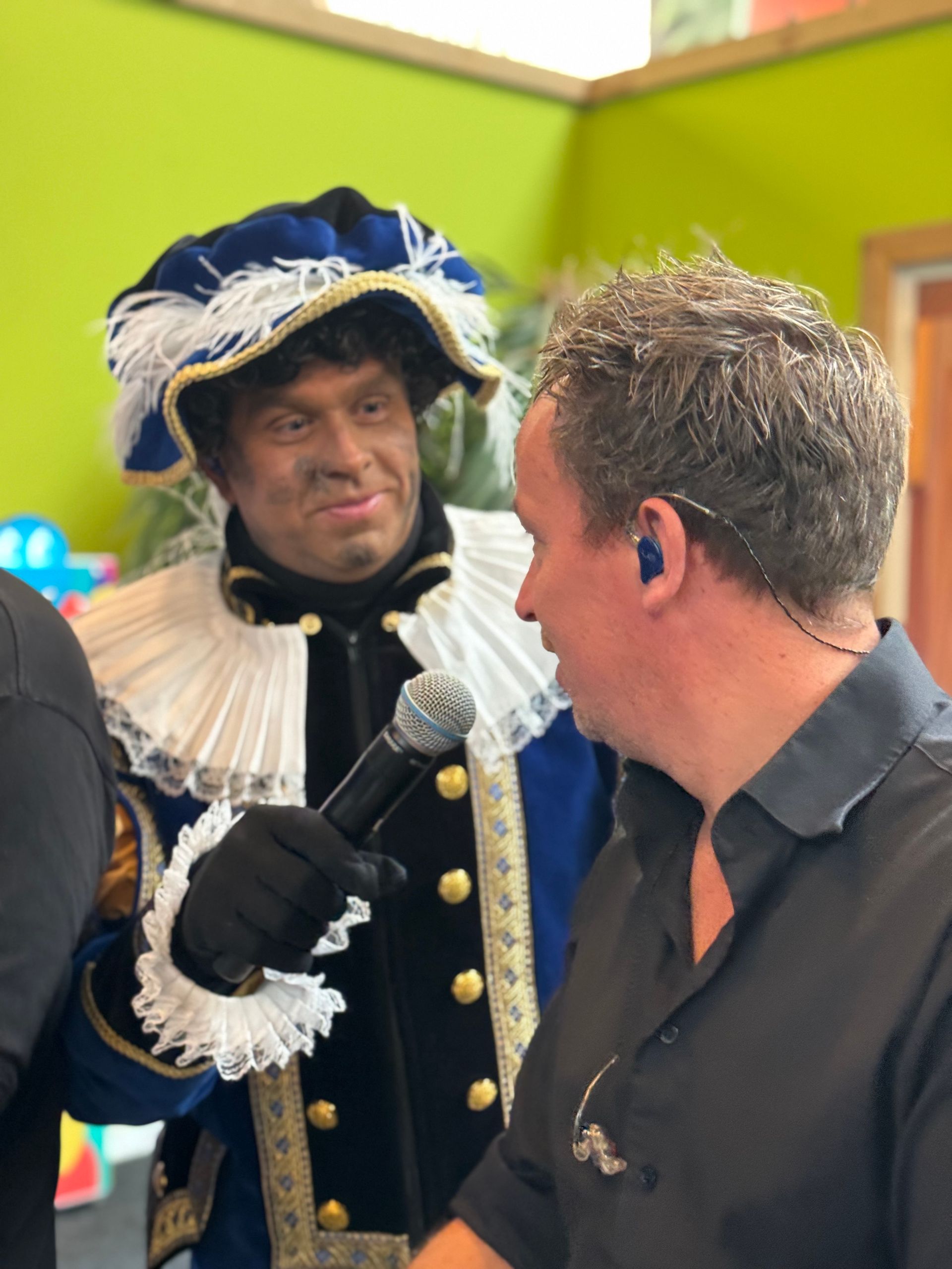 Een man in een kostuum houdt een microfoon vast en praat met een andere man